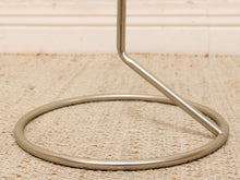 Load image into Gallery viewer, A close-up of a polished silver metal stand base with a circular ring and a diagonal support rod, resting on a beige woven rug.
