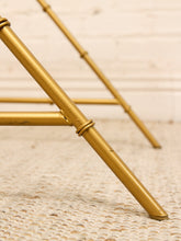 Load image into Gallery viewer, Close-up of a gold metal frame structure, likely furniture legs or a stand, resting on a textured cream rug against a light brick wall.
