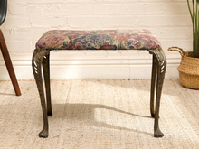 Load image into Gallery viewer, A vintage-style upholstered stool with a floral patterned seat cushion and dark carved cabriole legs, set on a woven rug against a white brick wall.
