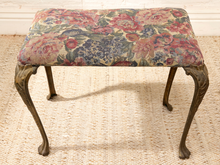 Load image into Gallery viewer, An antique-style upholstered stool with a floral patterned fabric seat cushion and carved dark wood cabriole legs, set on a woven beige rug.
