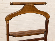 Load image into Gallery viewer, A close-up of a vintage wooden garment rack with a warm medium-brown finish, featuring a curved top bar, a lower shelf, and a white painted brick wall background.
