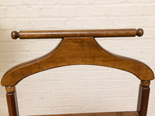 Load image into Gallery viewer, A close-up of a wooden chair backrest showing the curved back, turned legs, and a horizontal support rod with round finials, set against a white painted brick wall.
