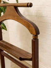 Load image into Gallery viewer, Close-up of a dark brown wooden hanger rack, showing the curved hanger bar, support post, and shelf against a white brick wall background.
