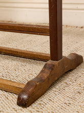 Load image into Gallery viewer, Close-up of the dark brown wooden base and leg of a vintage wooden table or stand, resting on a textured beige woven rug.
