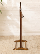 Load image into Gallery viewer, A vintage wooden coat rack with a dark brown vertical stand and a lighter brown base, set against a white brick wall on a beige woven rug.
