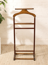 Load image into Gallery viewer, A vintage wooden garment stand with a curved top bar and three horizontal bars, shown against a white brick wall on a beige rug.
