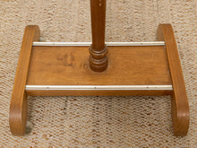 Load image into Gallery viewer, Close-up of the base of a wooden stand or rack with a medium brown finish, featuring curved side supports, a central column, and two horizontal metal guide bars, resting on a woven beige rug.

