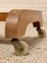 Load image into Gallery viewer, Close-up of a wooden furniture leg with casters, showing a curved medium-brown wood frame and two small off-white wheels on a woven beige rug.
