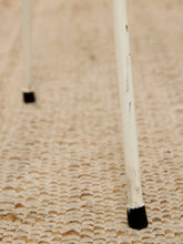 Load image into Gallery viewer, Close-up of white cane legs with black rubber tips standing on a beige woven rug.

