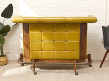 Load image into Gallery viewer, 1970s vintage rolling bar with Dijon mustard button-tufted upholstery, curved padded top rail, dark wood serving surface, and caster base
