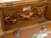 Load image into Gallery viewer, Close-up of the interior of an open vintage wooden trunk or chest, showing a brown satin-lined elastic pocket and painted floral detailing on the front.

