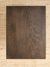 Load image into Gallery viewer, A rectangular dark brown wood panel with prominent wavy grain patterns, centered on a textured beige woven background.
