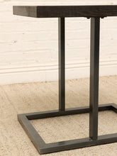 Load image into Gallery viewer, Close-up of a dark wood and dark metal side table on a beige textured rug against a white brick wall.
