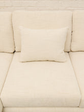 Load image into Gallery viewer, A cream-colored textured fabric sofa cushion with a matching square throw pillow resting on the seat of a matching sofa, set against a white brick wall background.
