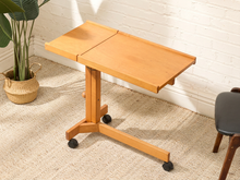 Load image into Gallery viewer, Vintage warm wood rolling C-table with rectangular two-part top, cantilevered base, raised back edges, and small caster wheels

