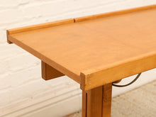 Load image into Gallery viewer, A close-up of a light brown wooden table showing the tabletop, corner joint, and leg against a white brick wall background.
