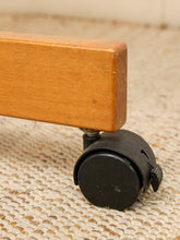 Load image into Gallery viewer, Close-up of a wooden furniture leg with a black caster wheel on a beige woven carpet.

