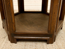 Load image into Gallery viewer, Close-up of a dark brown wooden hexagonal table or stand with visible wood grain and a woven beige surface underneath.
