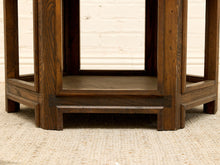 Load image into Gallery viewer, Close-up of the lower portion of a dark brown wooden table or shelf with a visible wood grain finish, standing on a light beige textured rug against a white brick wall background.
