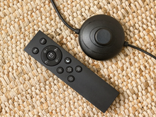 Load image into Gallery viewer, A black smart thermostat remote control and matching round wall mount receiver connected to a power cord, placed on a woven beige rug.
