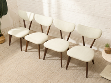 Load image into Gallery viewer, Five mid-century modern dining chairs with cream upholstered seats and curved wooden backs, arranged on a beige carpet against a white brick wall.
