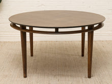 Load image into Gallery viewer, A round mid-century modern wooden dining table with a dark brown finish, featuring a double-ring support structure and four tapered legs, set against a white brick wall and light beige rug.
