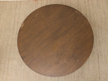 Load image into Gallery viewer, A round wooden board or lid with a dark brown wood grain finish, shown from a top-down view on a textured beige woven rug.
