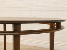 Load image into Gallery viewer, Close-up of a dark brown wooden table showing the tabletop edge, support legs, and a curved lower shelf against a white brick wall background.
