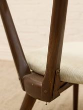 Load image into Gallery viewer, Close-up of a mid-century modern wooden dining chair with a dark brown wood frame, a cream upholstered seat, and visible metal hardware.
