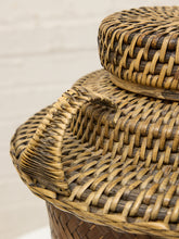 Load image into Gallery viewer, Close-up of a woven natural fiber basket with a matching lid, showing the detailed texture and interlaced pattern of tan and brown fibers.
