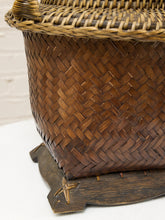 Load image into Gallery viewer, Close-up of a brown woven basket with a dark wooden base, showing the detailed hand-woven texture and part of the woven lid.
