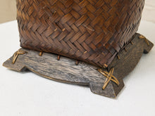 Load image into Gallery viewer, Close-up of a dark brown woven basket resting on a rustic dark wood stand with small tan leather ties, set on a white textured surface.
