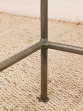 Load image into Gallery viewer, Close-up of a metal tripod-style stand or frame leg with a round base, resting on a woven beige rug.
