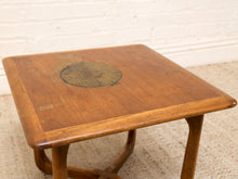 Load image into Gallery viewer, A square wooden side table with a warm medium-brown finish, featuring a circular inlay on the tabletop and a curved wooden base, set against a white brick wall and light beige carpet.
