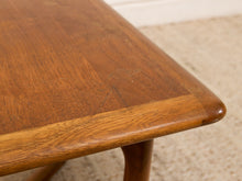 Load image into Gallery viewer, Close-up of a mid-century modern wooden table corner showing the rich grain of the teak wood, with a beige carpeted floor in the background.
