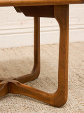 Load image into Gallery viewer, Close-up of a mid-century modern wooden table leg with a curved, tapered design and a central cross-brace, resting on a textured beige rug.

