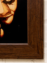 Load image into Gallery viewer, Close-up of a framed artwork showing part of a portrait with dark wood grain frame against a white wall.
