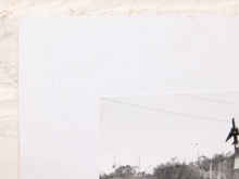 Load image into Gallery viewer, A close-up of a white sheet of paper or cardstock placed against a textured off-white wall, with a small corner of a black-and-white printed photograph visible in the lower right.
