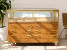 Load image into Gallery viewer, Vintage burl wood rolling display cabinet with glass showcase top, brass-tone trim, six drawers with brass pulls, and caster wheels
