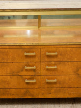 Load image into Gallery viewer, A close-up of a mid-century modern wooden dresser with a burl wood finish, six drawers with brass pulls, and a matching wood top with a glass-front upper cabinet section.

