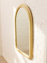 Load image into Gallery viewer, An arched wall mirror with a thick, ornate gold frame, mounted on a white painted brick wall.
