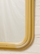 Load image into Gallery viewer, A close-up of a vintage-style rectangular mirror with a thick, curved mustard yellow frame, mounted on a white brick wall.

