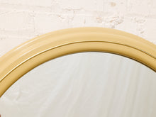 Load image into Gallery viewer, A close-up of a round wall mirror with a curved, ribbed frame in a warm mustard yellow or ochre color, set against a white painted brick wall.
