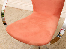 Load image into Gallery viewer, Close-up of a modern office chair with a peach-colored suede or velvet upholstered seat and curved chrome metal arms, set on a beige carpet.
