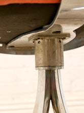 Load image into Gallery viewer, Close-up of a vintage metal stool base with a brushed silver cylindrical column and three curved legs, attached to a dark seat cushion.

