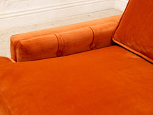 Load image into Gallery viewer, Close-up of an orange velvet armchair showing the tufted armrest and cushion, with a white baseboard and light floor visible in the background.
