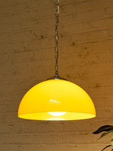 Load image into Gallery viewer, A glowing yellow dome pendant light hanging from a metal chain against a warm beige brick wall.
