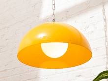 Load image into Gallery viewer, A glossy yellow dome pendant light hanging from a silver chain against a white brick wall.
