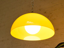 Load image into Gallery viewer, A modern dome-shaped pendant light with a glossy yellow shade and a glowing white bulb inside, hanging from a silver chain against a textured brick wall.
