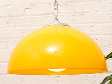 Load image into Gallery viewer, A glossy yellow dome pendant light shade hanging from a silver metal chain against a white brick wall background.
